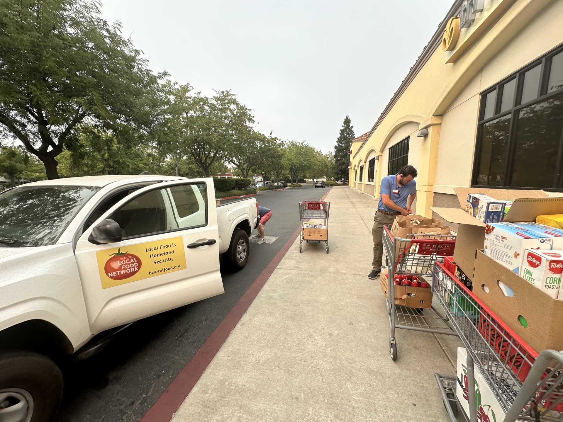 A volunteer loading boxes of donated groceries into carts beside a Butte County Local Food Network pickup truck outside a Chico grocery store.